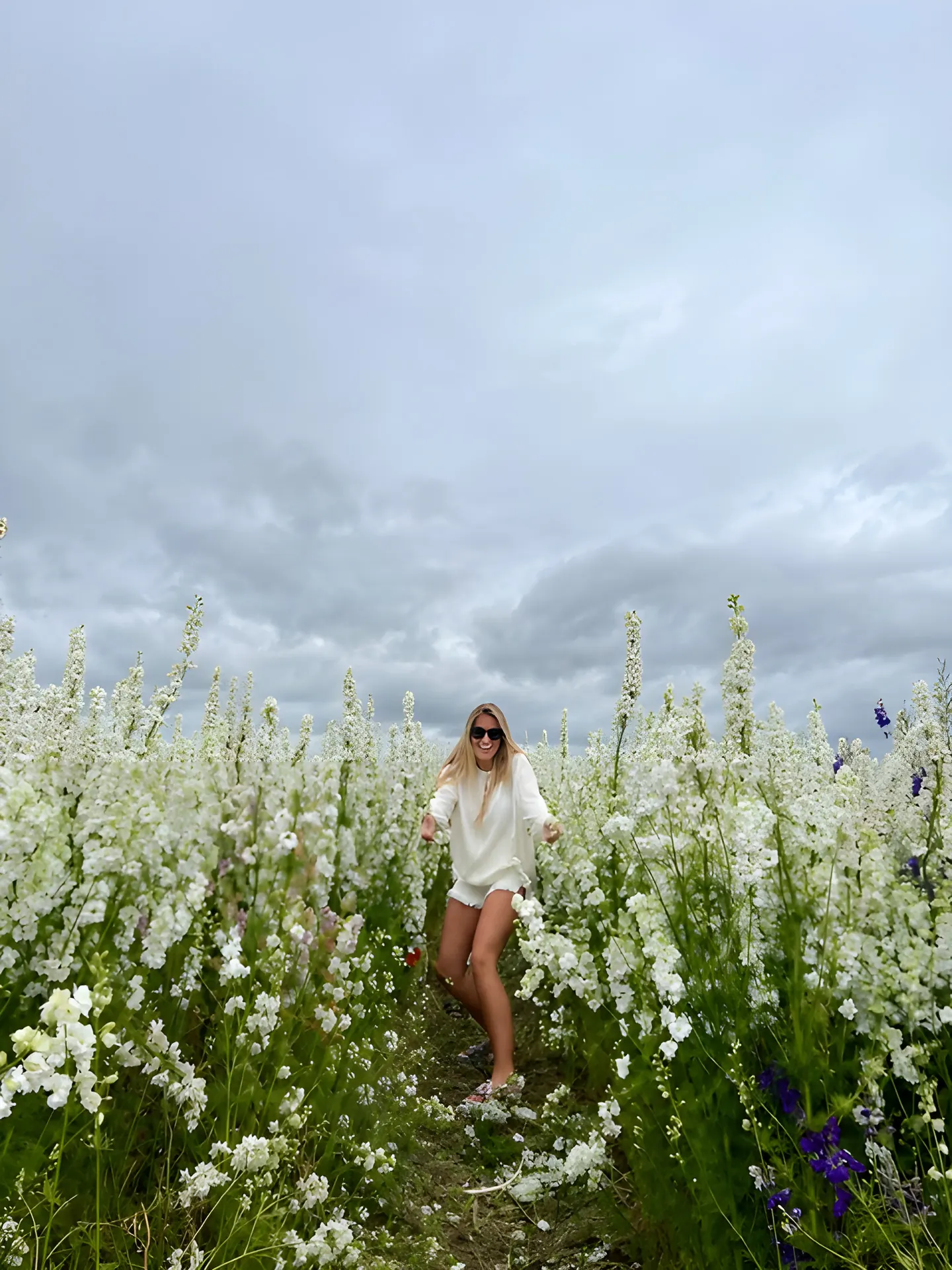 Hayley walking through a field of white flowers under a wide sky